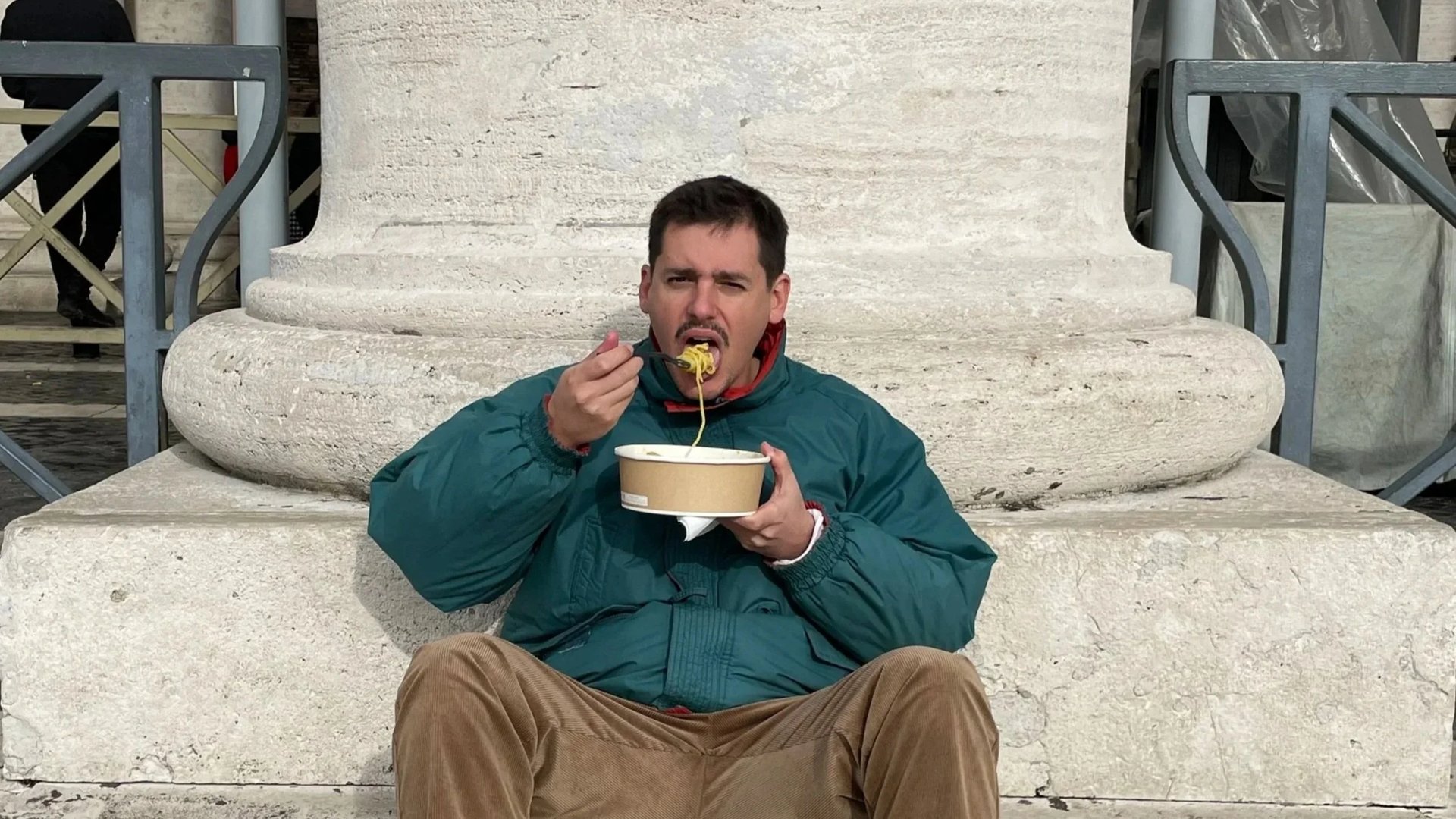 Mario Gismera eating pasta by a stone column